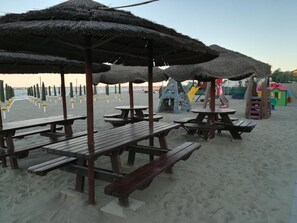 A beach with picnic tables and umbrellas, a playground, and a clear sky. - Aurora Residence (Ravenna)