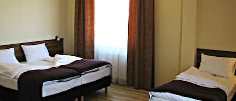 A hotel room with two beds, wooden flooring, and a window with curtains.