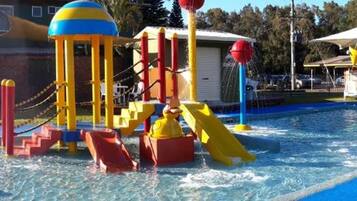 A swimming pool with a water play area and lounge chairs.