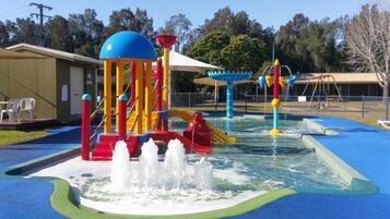 A water play area with a slide, splash pad, and a building in the background.