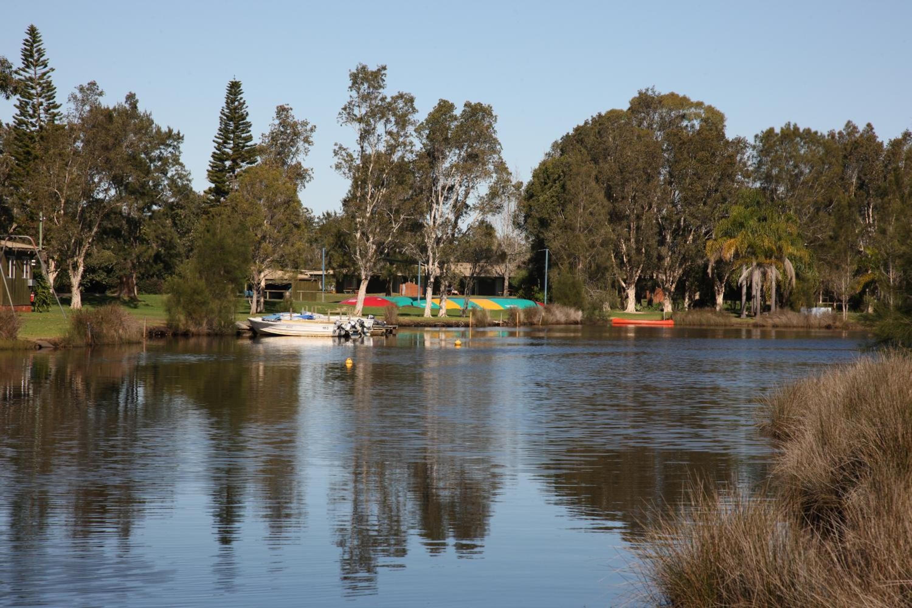 A calm lake with boats, trees, and a small building with a roof.