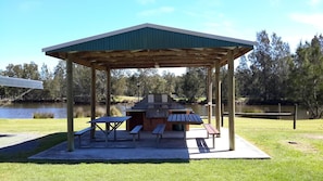 Un área de picnic techada con mesas, bancos, una parrilla y vistas a un lago.