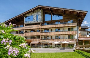Un immeuble à plusieurs étages doté d’une façade en bois, de balcons et d’un espace restaurant avec des places assises en plein air.
