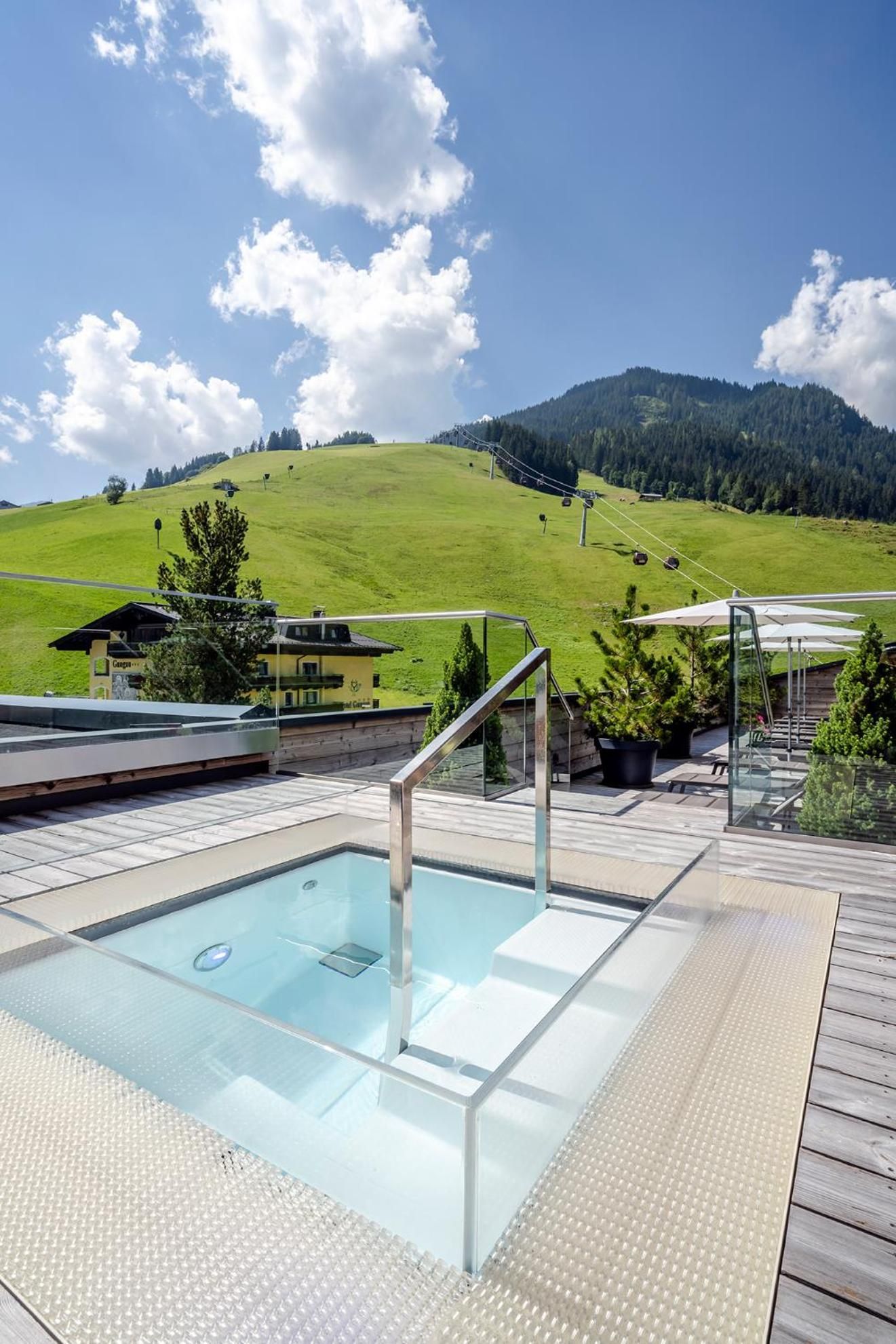 A clear blue sky with a pool area featuring a glass-enclosed pool, wooden deck, and a mountain view.