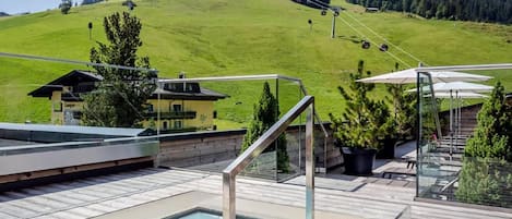 A clear blue sky with a pool area featuring a glass-enclosed pool, wooden deck, and a mountain view.