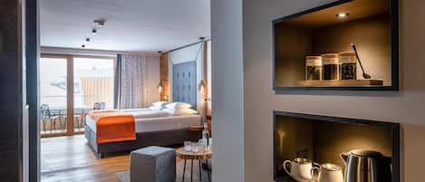 A modern hotel room with a bed, a dining area, and a kitchenette.