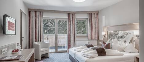 A hotel room with a bed, a desk, a chair, a window with curtains, and a view of the outdoors.