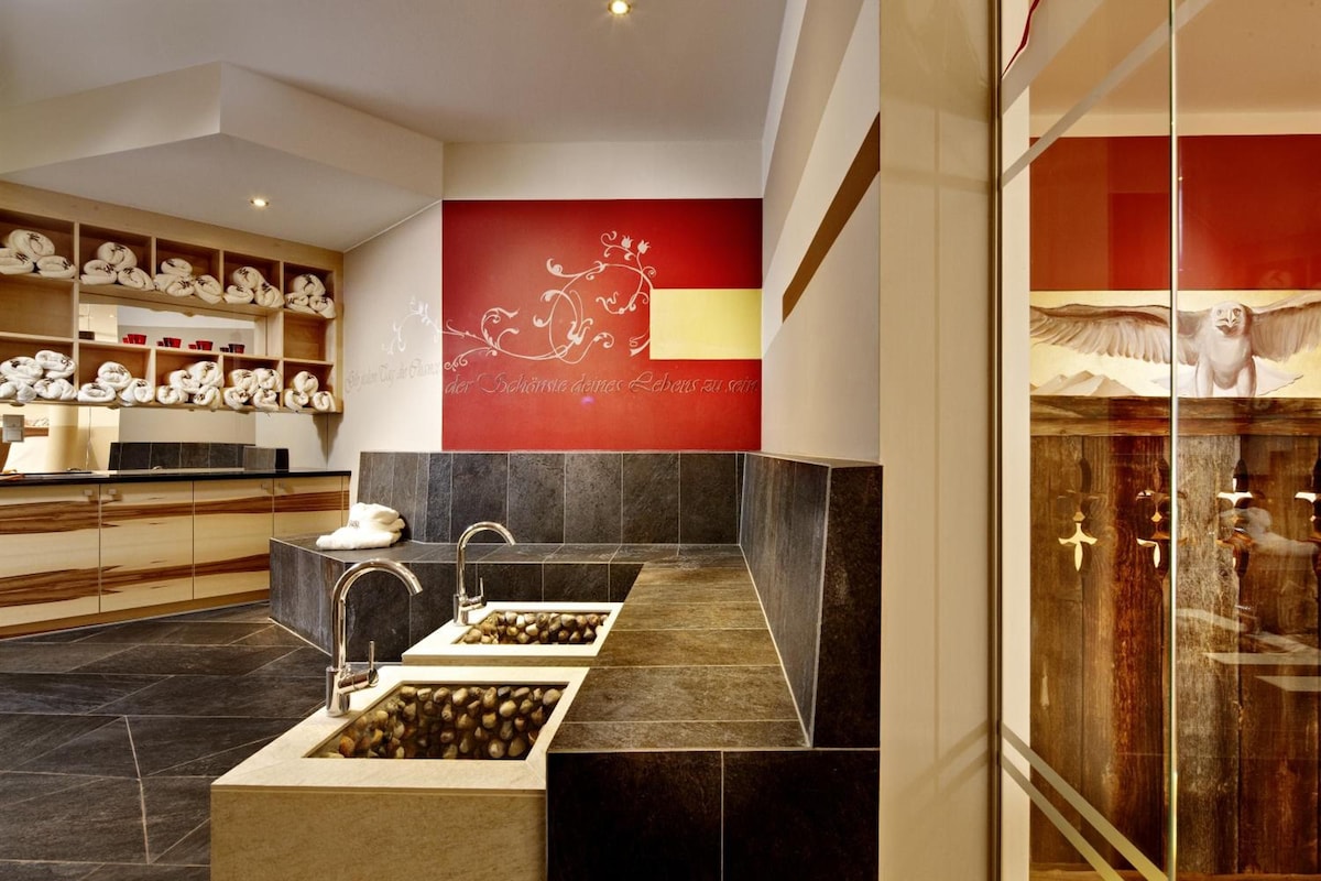 A modern bathroom with a dual sink, marble flooring, and a red accent wall with decorative script.
