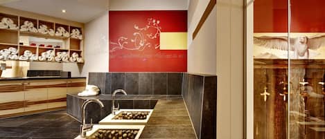 A modern bathroom with a dual sink, marble flooring, and a red accent wall with decorative script.