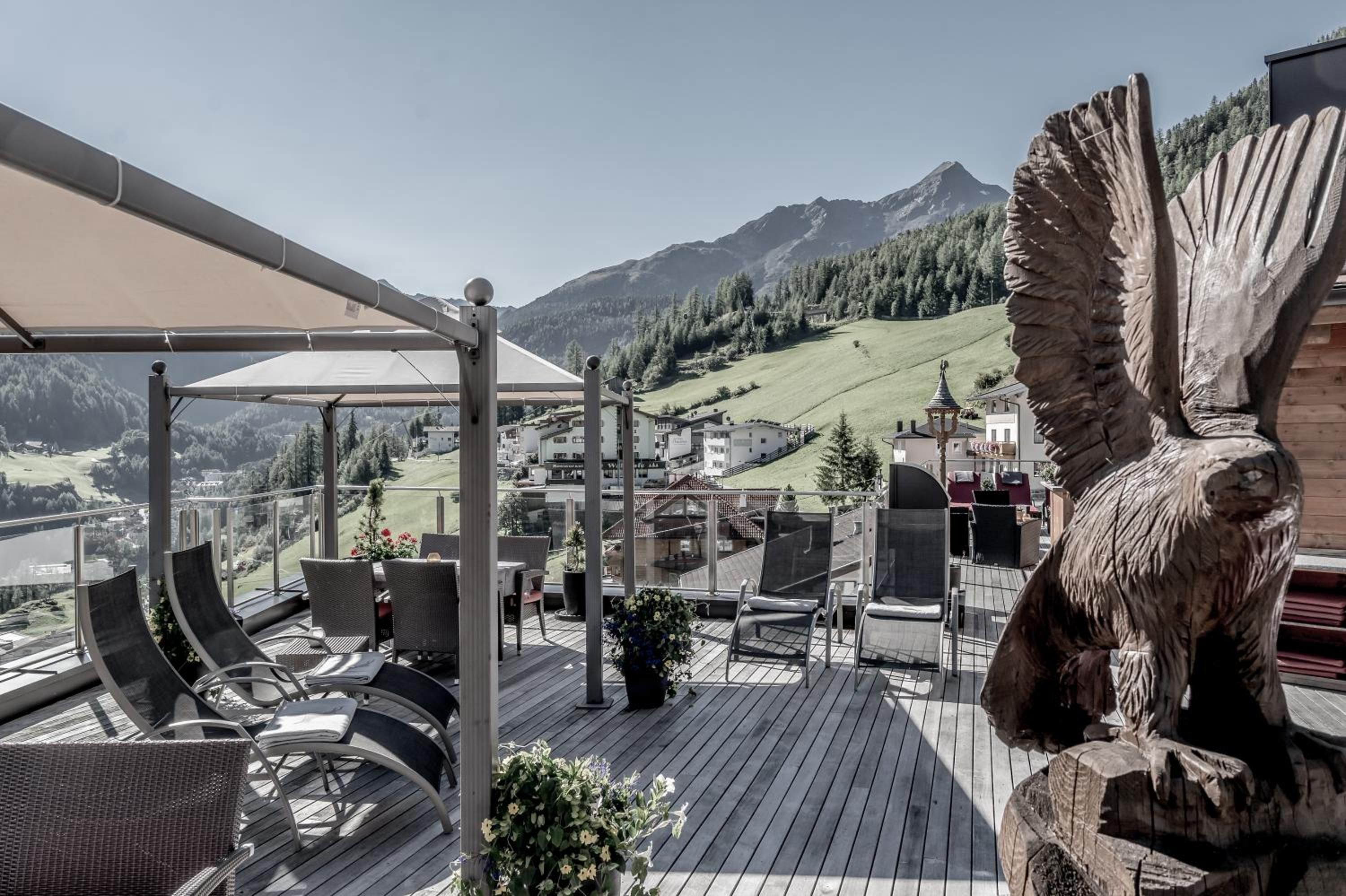 Una terraza con mesas al aire libre, una gran escultura de madera y vistas a un paisaje montañoso.