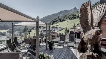 Eine Terrasse mit Sitzgelegenheiten im Freien, eine große Holzskulptur und Blick auf eine Berglandschaft.