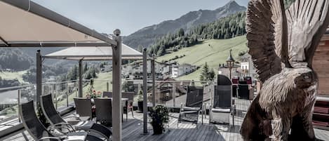 A terrace with outdoor seating, a large wooden sculpture, and a view of a mountain landscape.