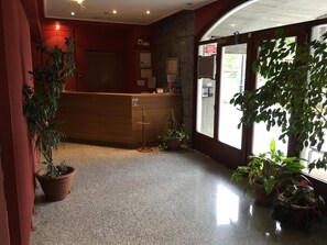 A reception area with a wooden desk, potted plants, and a large window. - Hotel Errekagain (Guenes)