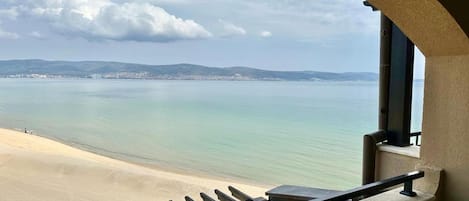 Une vue depuis un balcon doté d’une balustrade, donnant sur une plage et un paysage urbain lointain.