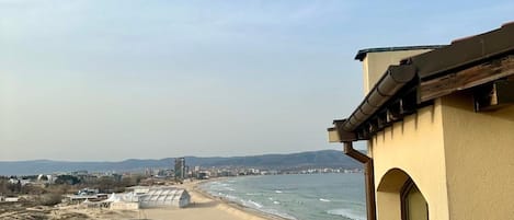 Vista costera con playa, océano y un horizonte urbano distante.