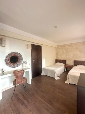 Ein Hotelzimmer mit zwei Betten, Holzboden, Schreibtisch mit Stuhl, Spiegel und einer Wanddekoration.