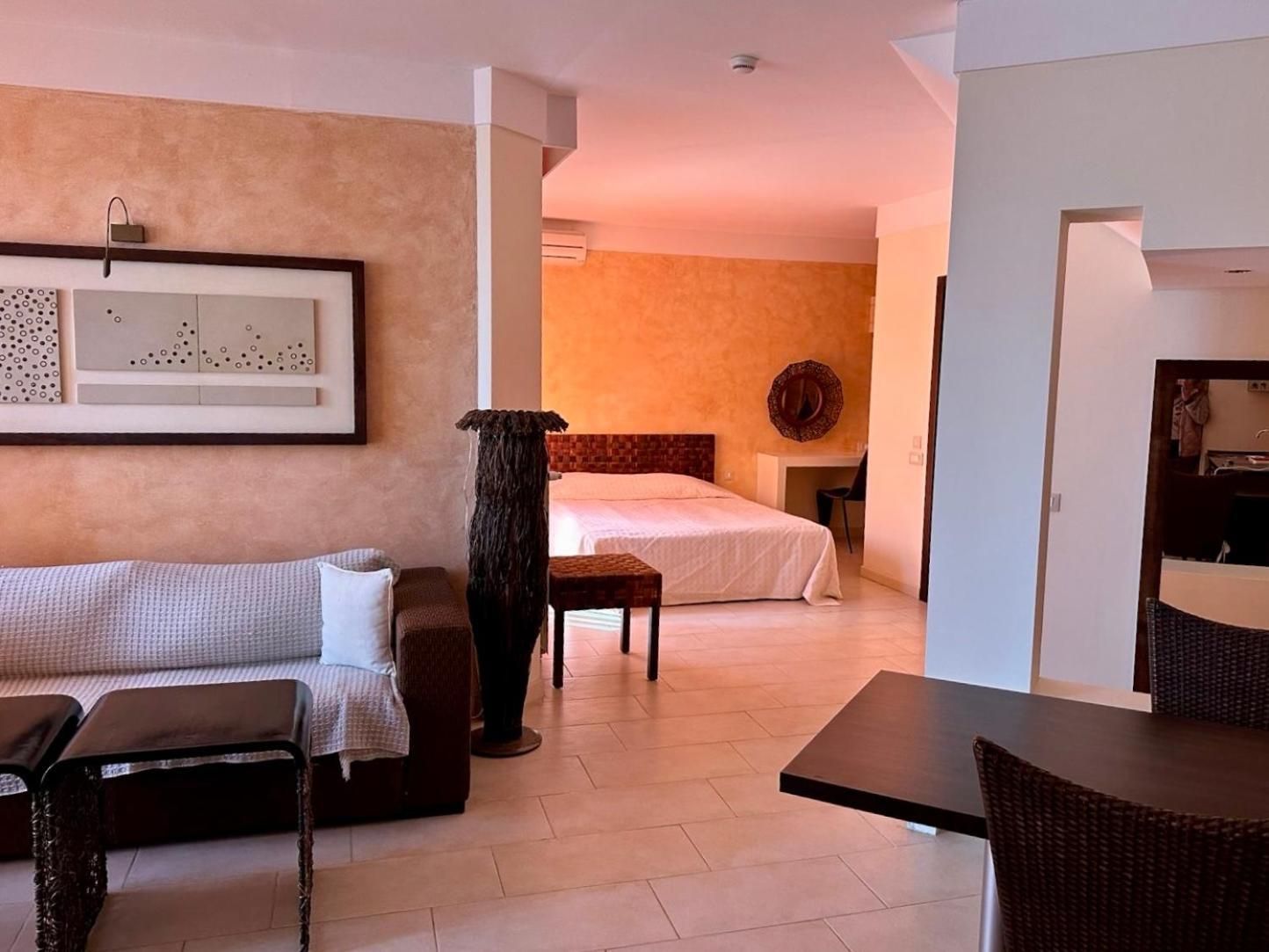 A hotel room with a bed, a sitting area with a sofa and a coffee table, and a dining area with a table and chairs.