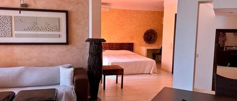 A hotel room with a bed, a sitting area with a sofa and a coffee table, and a dining area with a table and chairs.