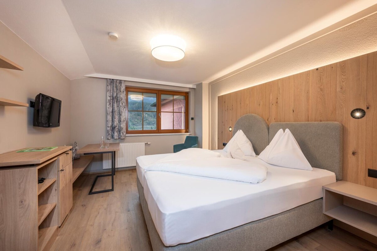 A hotel room with a bed, a desk, a chair, a television, and a window with curtains.