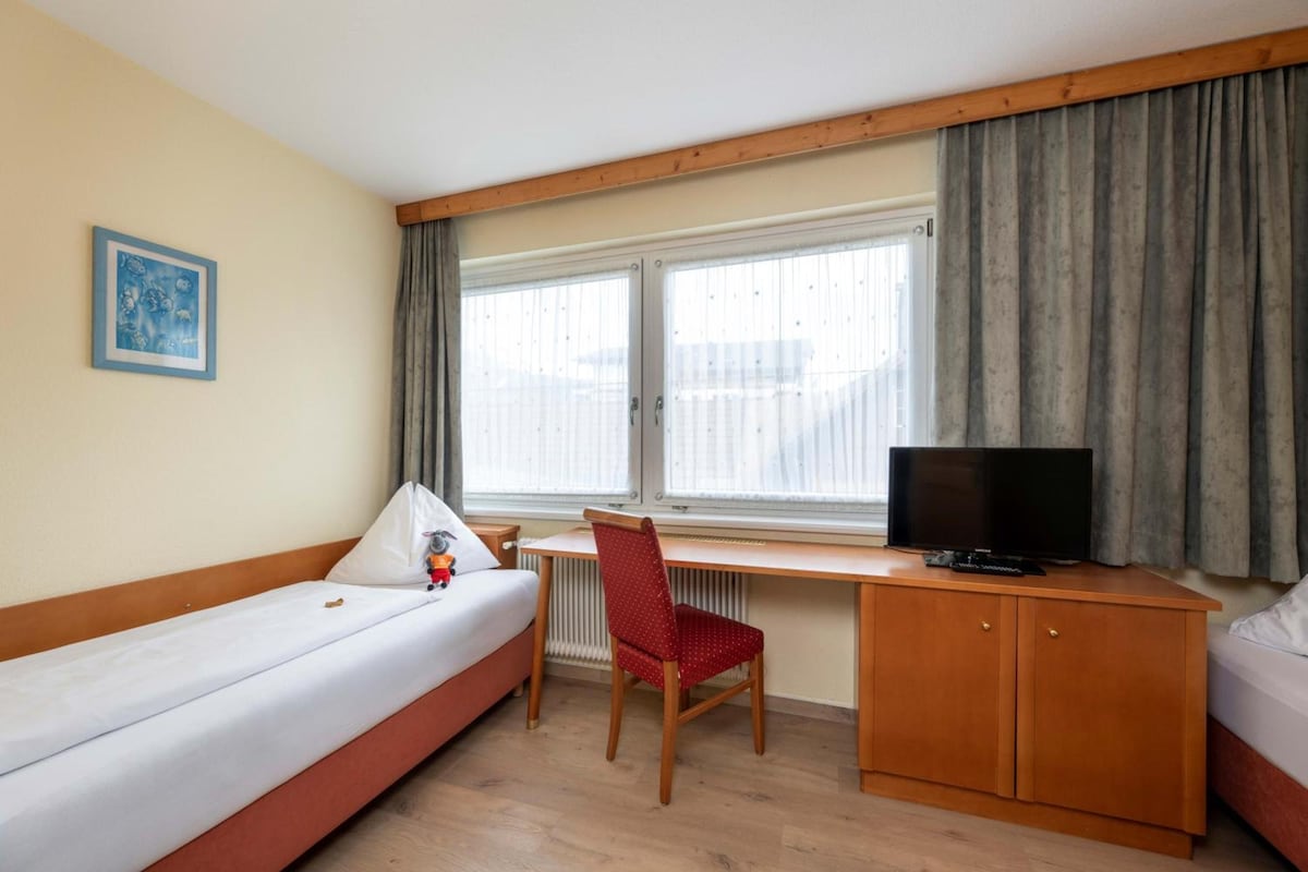 A hotel room with a bed, a desk with a chair, a television, and a window with curtains.
