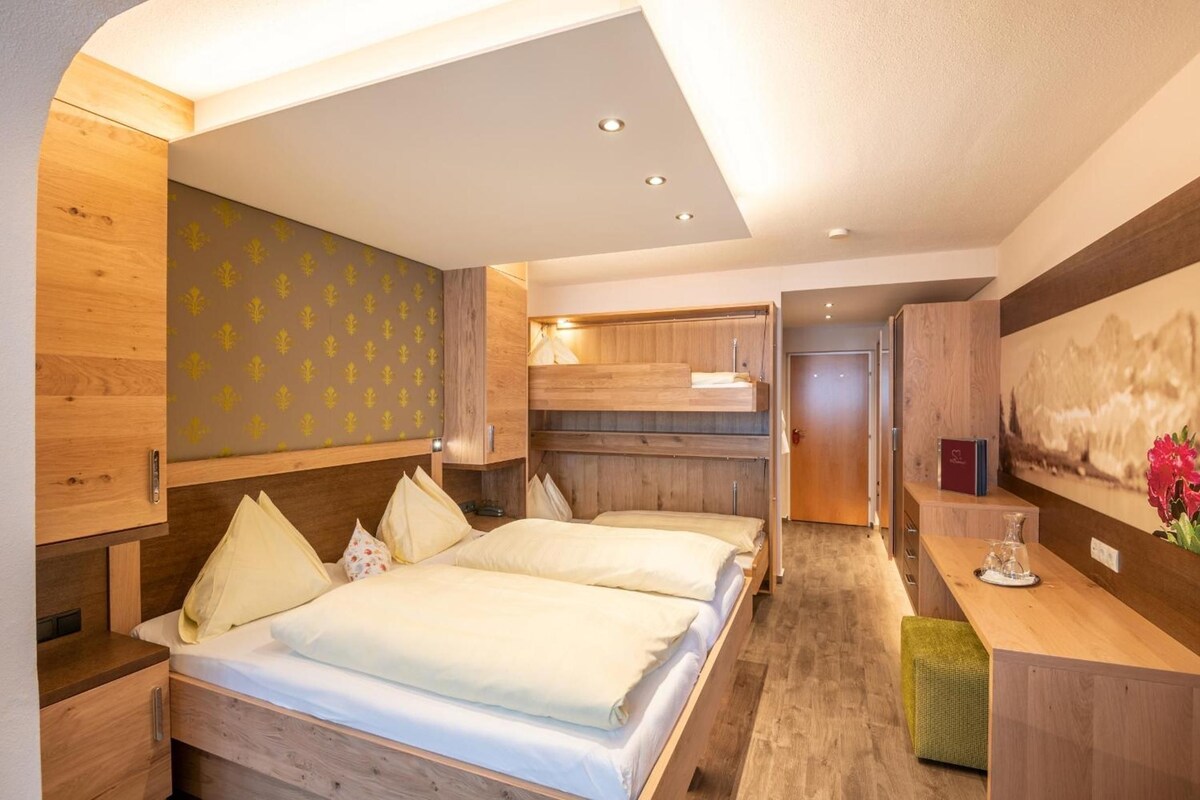 A hotel room with a double bed, wooden headboard, a small desk, and a painting on the wall.