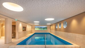 A large indoor swimming pool with a clear view of a mountainous landscape through a large window. - Bliem S Familienhotel (Haus)