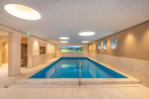 Una amplia piscina interior con vistas despejadas a un paisaje montañoso a través de un gran ventanal.