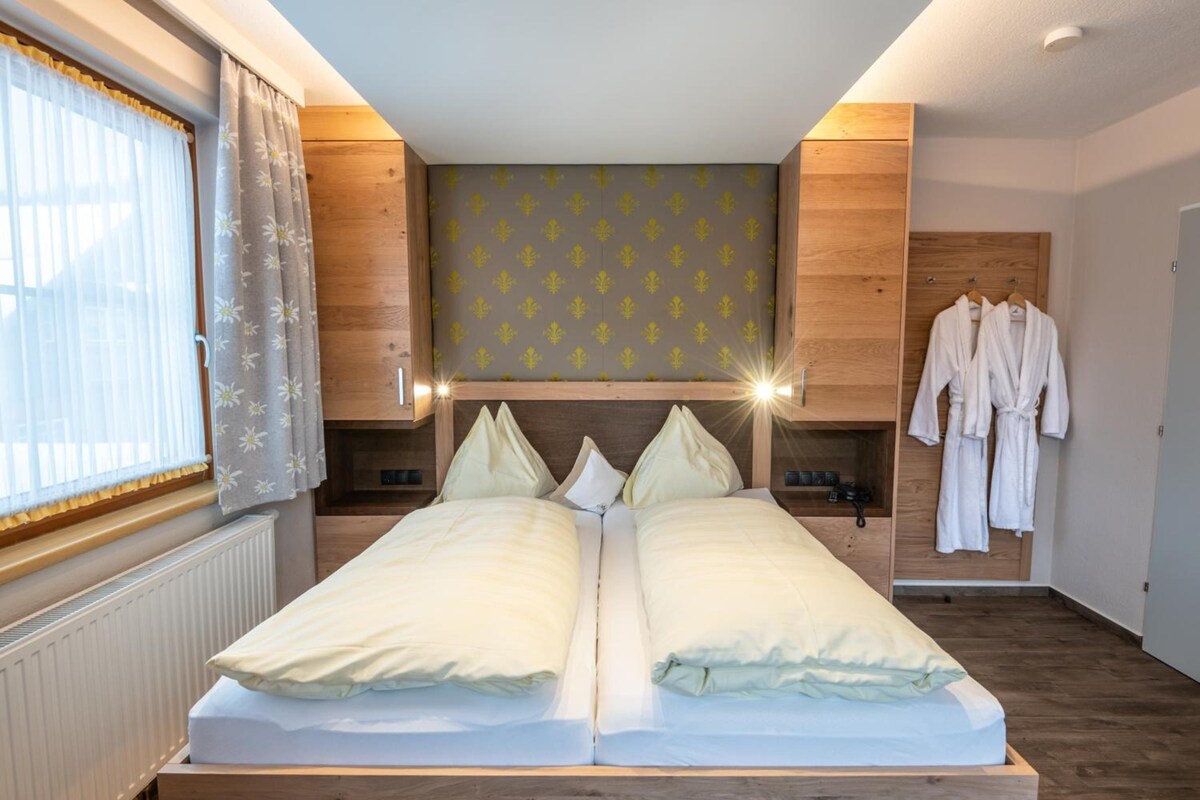A double bed with a headboard, bedside tables, and a robe rack in a hotel room.