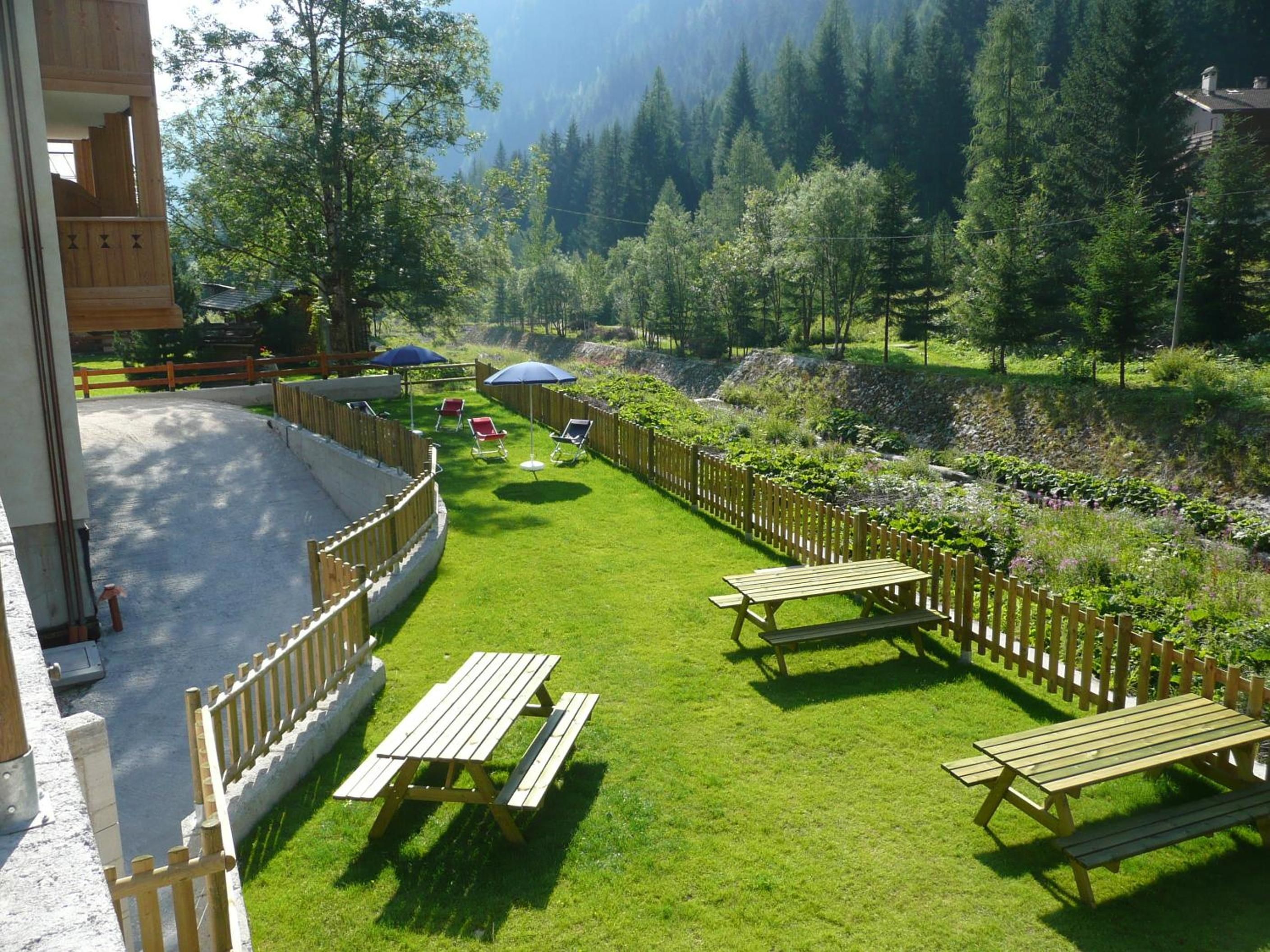 Un espace extérieur verdoyant, avec des tables de pique-nique et des parasols, entouré d’une clôture en bois et d’arbres.