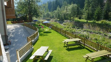 Ein grünes Freigelände mit Picknicktischen und Sonnenschirmen, umgeben von einem Holenzaun und Bäumen.