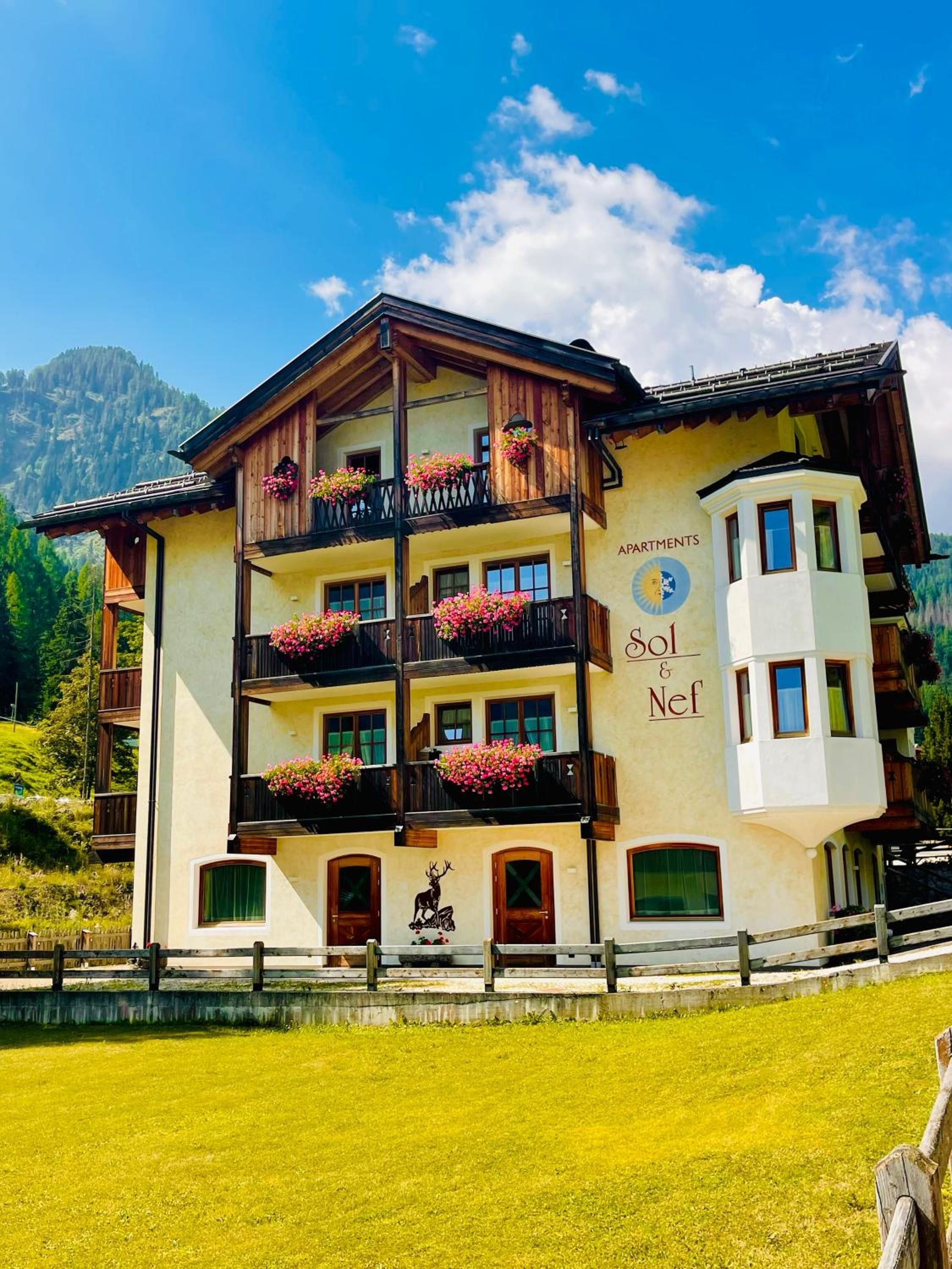A multi-story building with balconies, a mountain backdrop, and a sign indicating 'APARTMENTS Sol & Nef.'