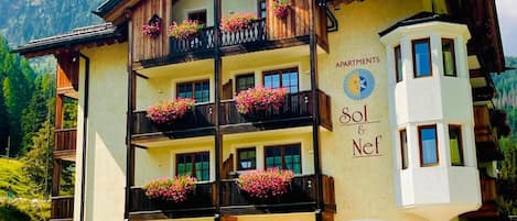 A multi-story building with balconies, a mountain backdrop, and a sign indicating 'APARTMENTS Sol & Nef.'