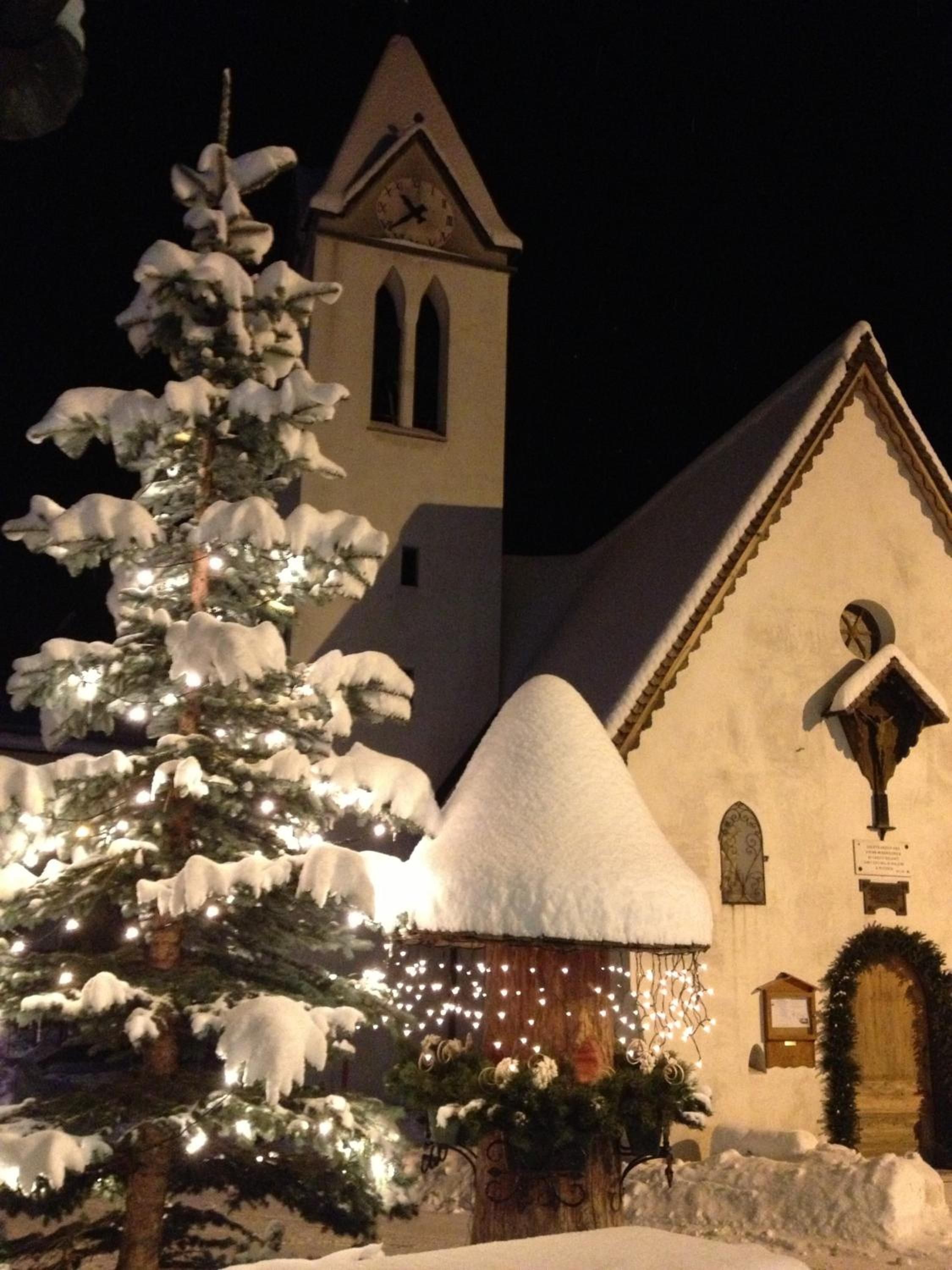 Een met sneeuw bedekte kerk met een klokkentoren en een sneeuwbedekte boom ervoor.
