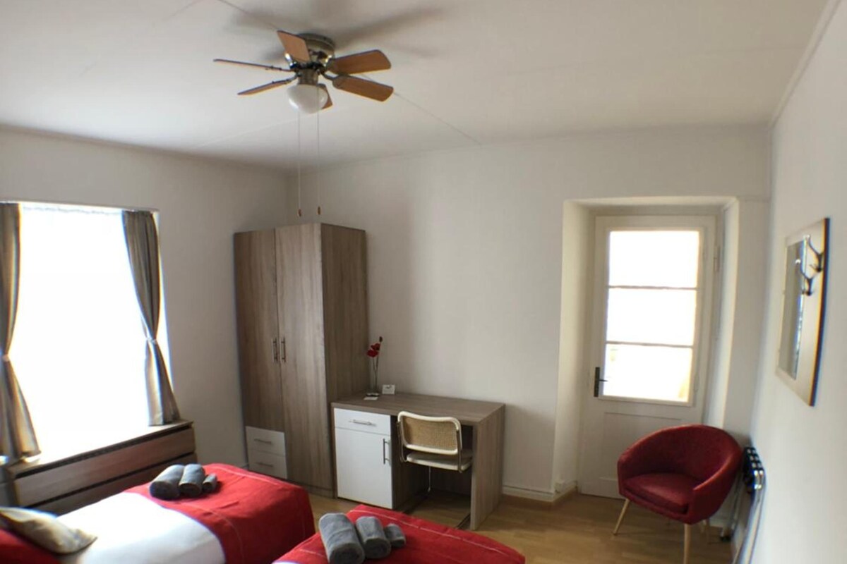 Habitación de hotel con dos camas, un escritorio, una silla, un armario y un ventilador de techo.