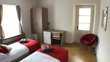 Ein Hotelzimmer mit zwei Betten, einem Schreibtisch, einem Stuhl, einem Kleiderschrank und einem Deckenventilator.