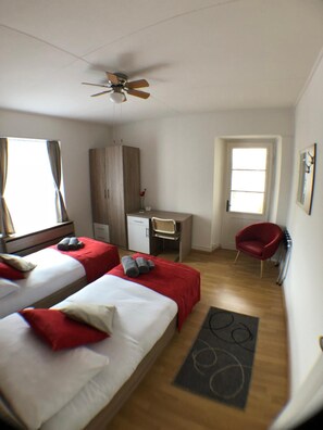 Habitación de hotel con dos camas, un escritorio, una silla, un armario y un ventilador de techo.