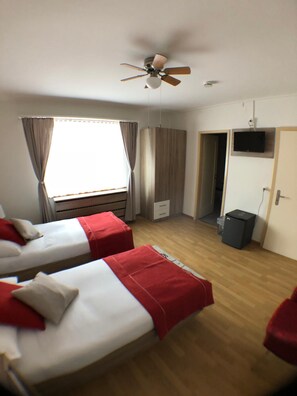 Una habitación de hotel con dos camas, ventilador de techo, televisor y armario.
