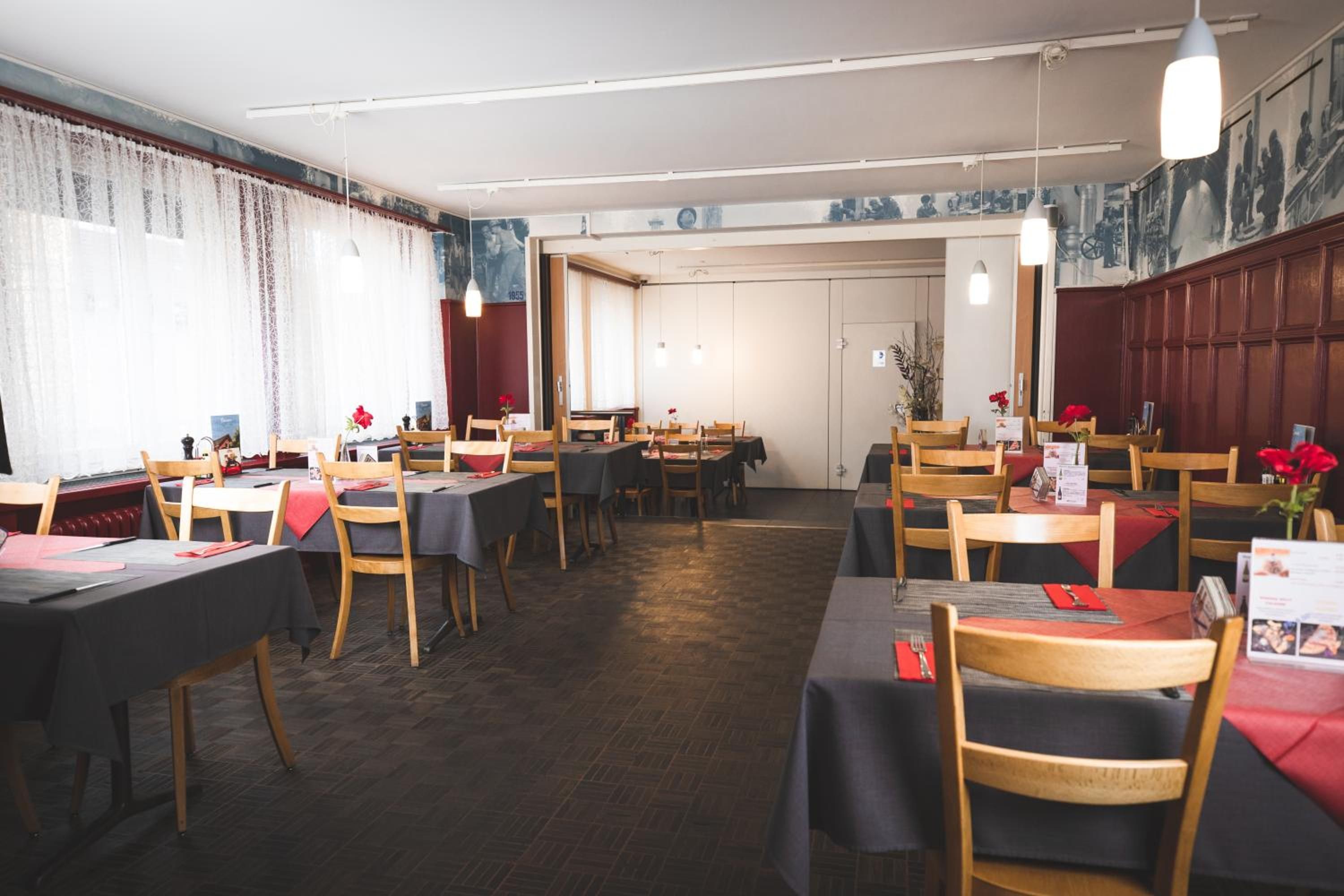 Ein Restaurant mit mehreren Tischen und Stühlen, Holzböden und einer Mischung aus natürlicher und künstlicher Beleuchtung.