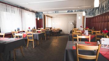 Ein Restaurant mit mehreren Tischen und Stühlen, Holzböden und einer Mischung aus natürlicher und künstlicher Beleuchtung.