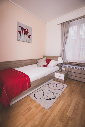 Un dormitorio con cama, mesita de noche, lámpara y ventana con cortinas.