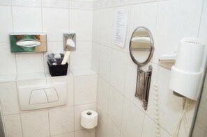 Un baño con secador de manos, espejo, dispensador de toallas y porta papel higiénico.