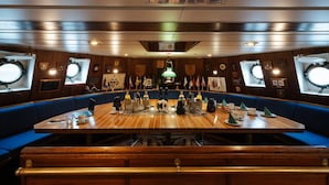 A dining area with a long wooden table, blue upholstered benches, and various dining items. - Alexander Von Humboldt Das Schiff (Bremen)