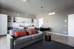 A modern living room with a grey sofa, a coffee table, and a dining area with a table and chairs. - Dreams Hotel Cittv Studi (Milan)