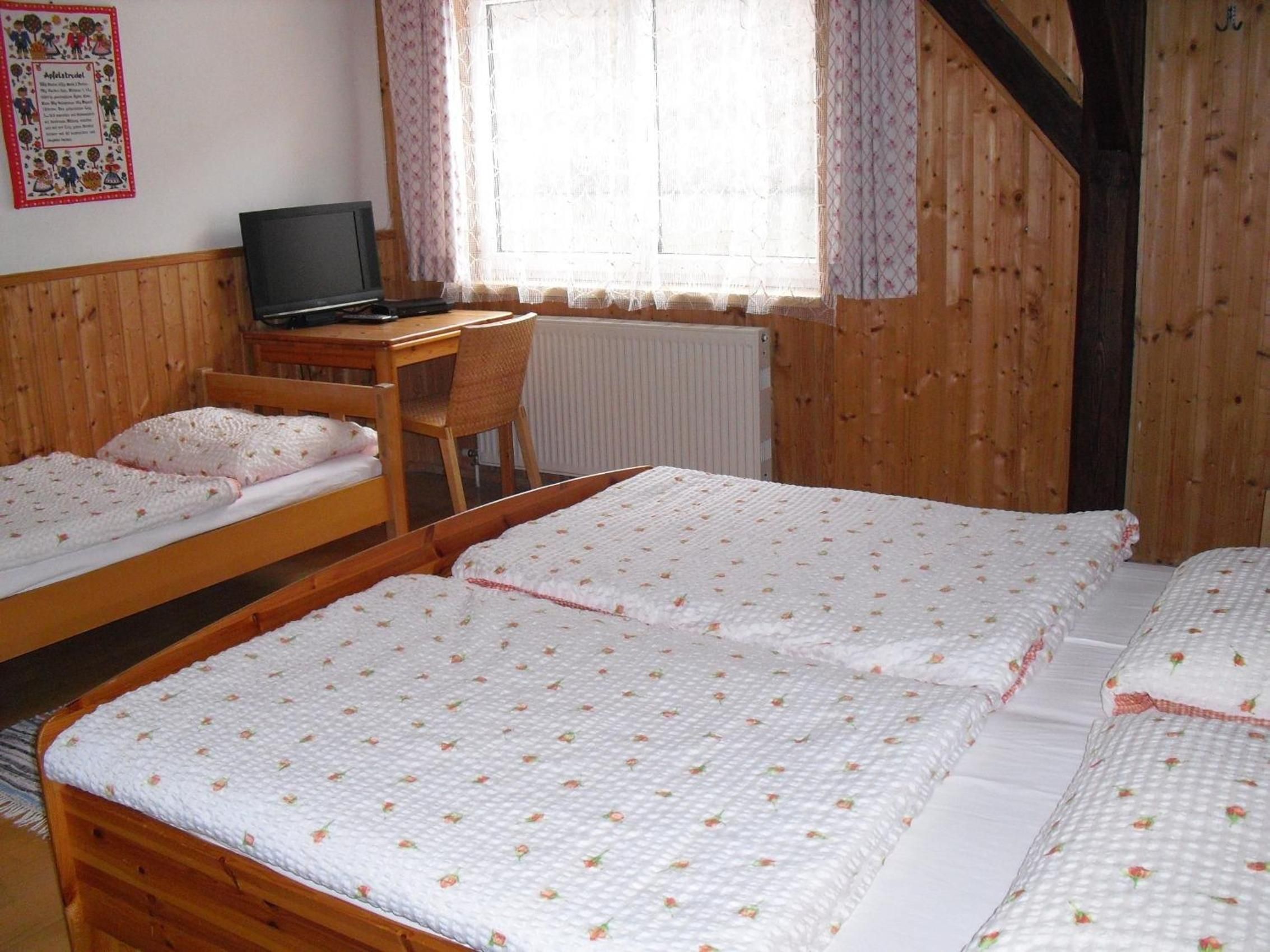 Ein Zimmer mit zwei Holzbett, einem Schreibtisch mit Computer und einem Fenster mit Vorhängen.