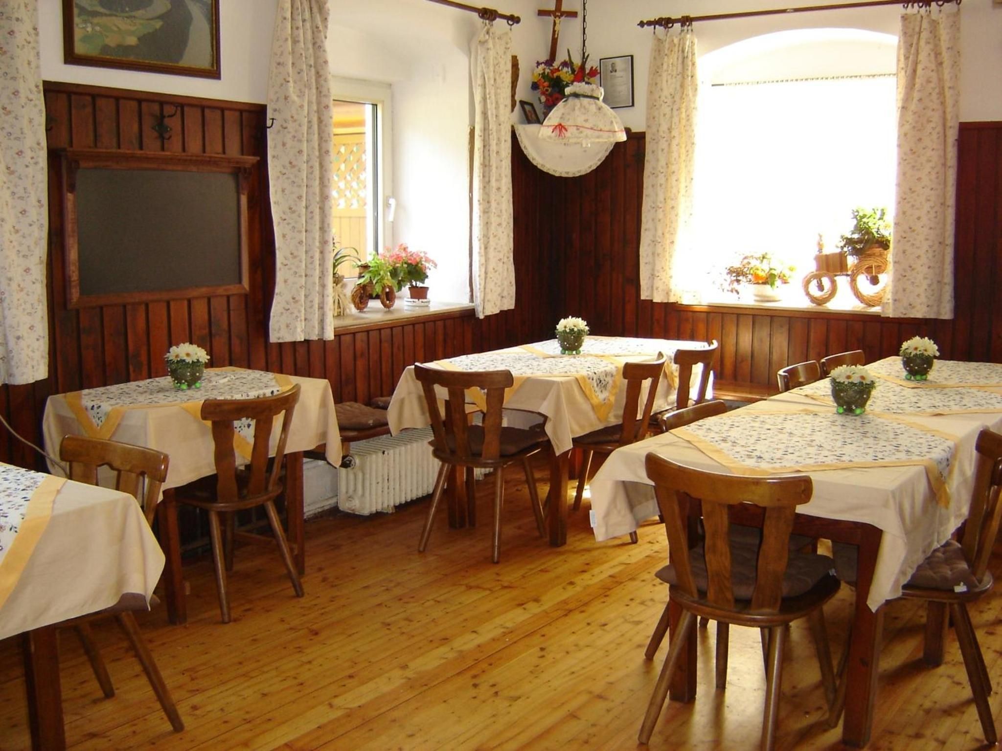 Ein Essbereich mit Holztischen und -stühlen, floralen Tischdekorationen und Blick ins Freie durch Fenster.