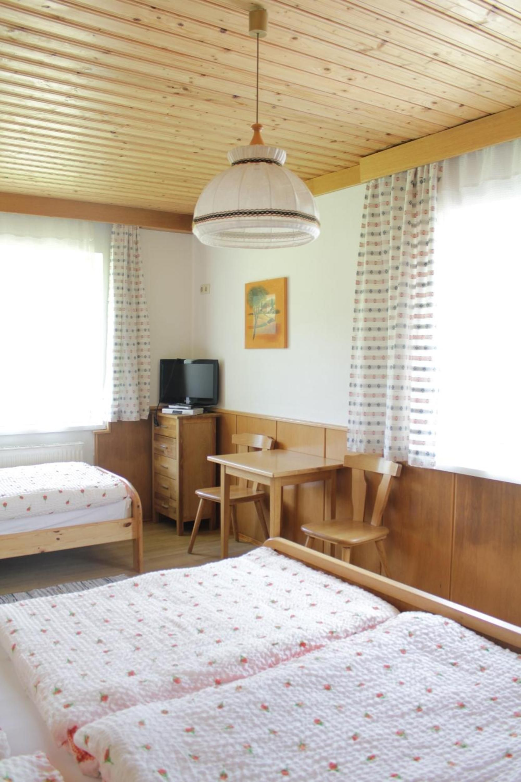 Ein Zimmer mit zwei Betten, einem Schreibtisch, einem Stuhl, einem Fernseher und einem Bild an der Wand.