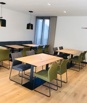 Una sala conferenze moderna con diversi tavoli e sedie, ampie finestre con tende e illuminazione a soffitto.