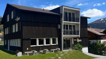 Un immeuble de deux étages avec une façade sombre, de grandes fenêtres et un balcon à l’étage supérieur.