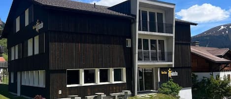 A two-story building with a dark facade, large windows, and a balcony on the upper floor.