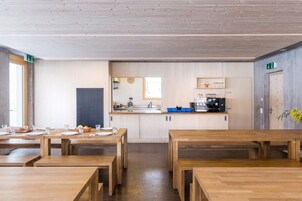 Una cocina moderna con armarios de madera, una cafetera y un lavabo. Hay mesas y bancos de madera dispuestos para comer.